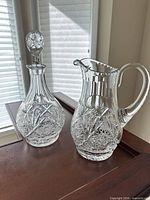 Decanter with stopper beside matching pitcher on table