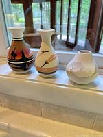 Three pottery vases lined on windowsill showing size and decoration