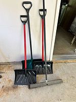 Three snow shovels and push broom leaning against wall