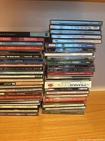 Two vertical stacks of compact discs on a wooden surface showing quantity and variety