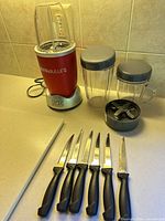 Blender base, three cups, lids, blade assembly, six knives on countertop