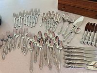 Flatware pieces spread out showing forks, spoons, knives, serving utensils and wooden chest