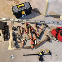 Entire assortment laid out: toolbox, level, framing square, hammers, pliers, knee pads, clamps, tape measure, flashlight