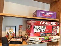 Shelf with Balderdash, board game stack, Wizard of Oz VHS, Monopoly box, domino case