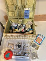 Open wicker sewing box showing interior satin lining and contents including thread spools, needles in packaging, organizer tray, pins