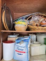 Overview of shelves with flour bag, plastic containers, metal pan, baskets and wooden bowls