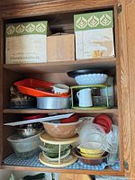 Cabinet shelf showing boxes, roasting pan, milk glass bowl on riser, ceramic pitcher, mixing bowls, lazy Susan