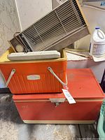 Stacked orange Thermos cooler on red metal chest cooler with small electric heater/fan on top