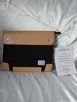 Front view of black canvas sleeve with tan leather flap and trim, brand label visible