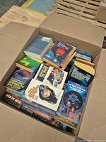 Open box showing assortment of mass-market paperback books, spines and covers visible