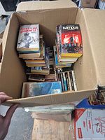 Open box showing stacks of paperback novels with titles such as There Is No Darkness and Kampus visible