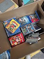Box full of assorted Blu-ray and DVD cases, several titles visible