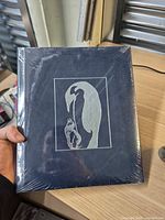 Front view of sealed hardcover photobook with penguin silhouette artwork