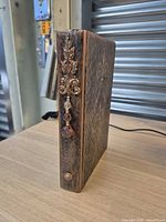 Spine view showing metallic floral applique, dangling bead, and textured cover