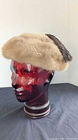 Tan fur pillbox hat with tassel on mannequin head
