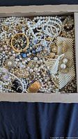 Top view of box showing mix of faux pearl jewelry, gold-tone bangle, pendant, earrings, and bead pieces