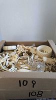 Open box filled with assorted cream and gold-tone costume jewelry pieces