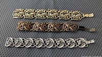 All three bracelets laid out: gold-tone, brown carved, silver-tone