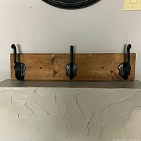 Front view showing wood backboard and three black hooks