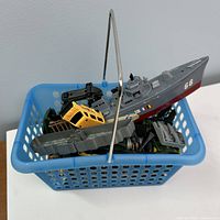 Basket filled with assorted toy vehicles; visible naval ship, helicopter, yellow SUV