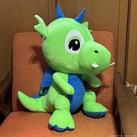 Front view of green and blue dragon plush on chair