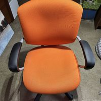 Front view showing orange upholstered backrest, seat, and fixed armrests