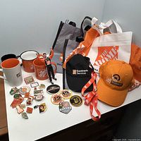 Overview showing caps, mugs, tote bags, pins, badges, lanyard and figurine