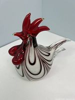 Front three-quarter view of glass rooster showing red comb, white body with dark red swirls, clear tail