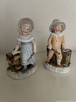 Front view of both bisque child figurines showing attire and pails