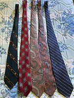 Five ties laid flat showing front patterns: green stripe, red geometric, two brown paisleys, navy geometric