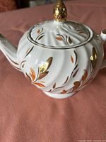Side view of teapot showing swirl body, floral gilding, finial