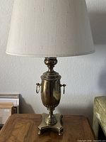 Full view of one brass table lamp with shade on wooden table