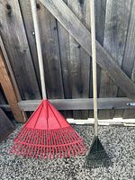 Both rakes leaning against fence