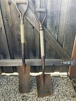 Both shovels leaning against fence