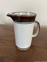 Front view of speckled stoneware pitcher with brown band, handle, spout