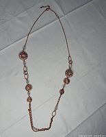 Full view of rose-gold tone long necklace laid flat showing disc arrangement and tassel