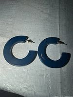 Blue C-shaped plastic hoop earrings with metal posts laid on fabric surface