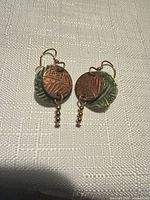 Front view of earrings showing copper-tone disc, green overlay, and dangling gold beads