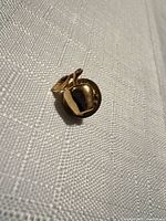 Front view of gold-tone apple pin on fabric backdrop