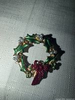 Front view of wreath brooch showing enamel leaves, faux pearls and red bow