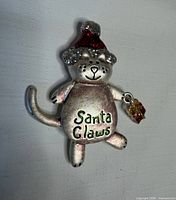 Front view of cat brooch showing hat, lettering and charm
