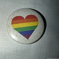 Front view of white round pin with rainbow heart graphic, shows coloration and surface wear