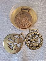 Three brass harness medallions including cased Foodland Ontario piece, map of Great Britain brass, and lion/Wales brass