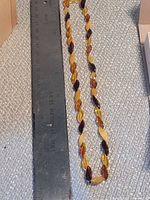 Full view of multicolor amber necklace beside ruler for length reference