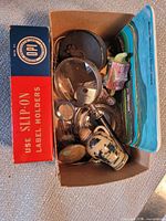 Top view of open box showing magnifying glass, measuring tape, vase, keys, brass tokens, postcards