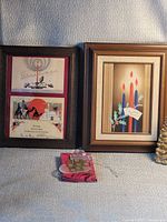 Two framed Christmas cards beside Tupperware ornament box and ornament