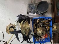 Blue plastic bin filled with various brass lamp parts including canopies, finials, wires and hardware
