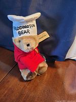 Full view of plush bear seated, showing red coat, white hat, and tags