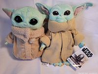 Front view of two Grogu plush toys with robes and eyes visible
