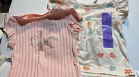 Both Calvin Klein girls tops laid flat showing front designs and size stickers